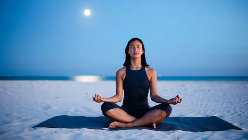 A person practicing yoga on a yoga mat on a quiet beach under the moonlight