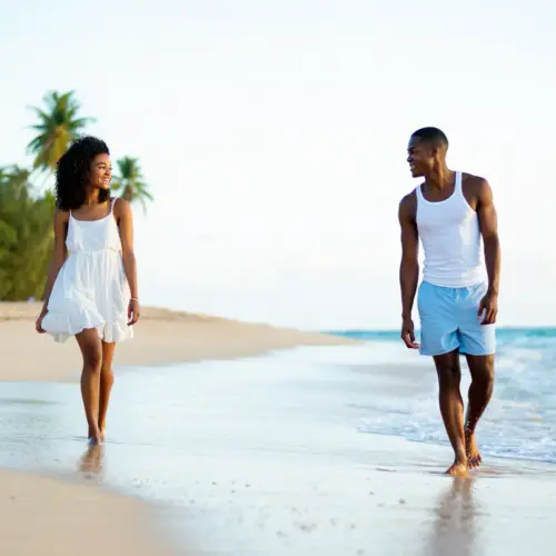 A couple walking on a sandy beach during sunset.
